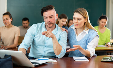 Man and woman students sitting at table, uisng laptop and discussing lesson.