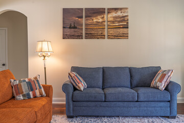 A living room with a blue couch and an orange chair. The couch is the main focus of the room and is surrounded by pillows. The room has a cozy and comfortable atmosphere