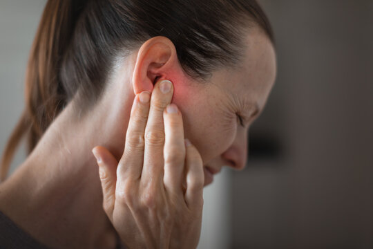 Young woman suffering from ear pain and tinnitus. Cause of earache includes otitis, earwax buildup.
