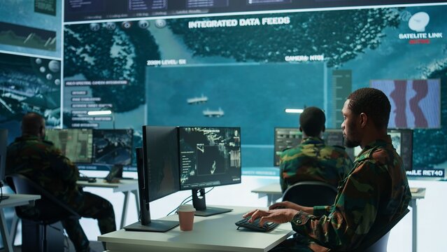 Team of military specialists overseeing surveillance activity by using a cctv footage and radar, pointing at a big screen and world map. High tech control center base of operations. Camera B.