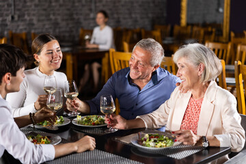 Elderly couple and young couple have dinner and drink wine together in restaurant