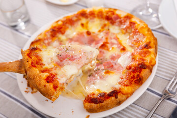 Cooked delicious pizza with stretchy cheese and prosciutto. Appetizing slice of Italian pizza on a plate close-up