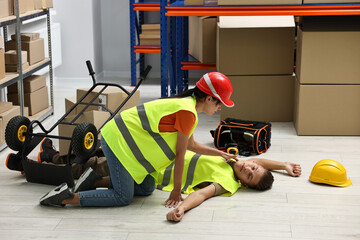 Accident at work. Woman checking pulse of her unconscious colleague in warehouse