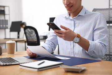 Man taking photo of document using scanning app on smartphone at desk in office, closeup