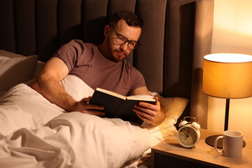 Young man reading book in bed at home