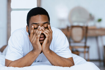 Sleepy African Man Rubbing Eyes Waking Up Lying In Bed At Home In The Morning. Insomnia Concept.