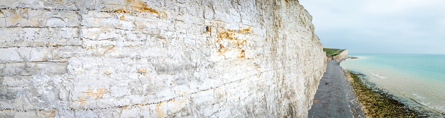 Seven Sisters chalk cliffs in the UK with dramatic coastal drop, tidal beach, and people walking along the shoreline