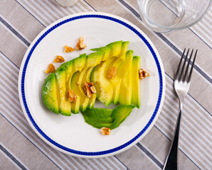 Appetizing ripe avocado slices served with walnuts to table..