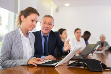 Young caucasian woman manager having conversation with her boss in meeting room during briefing and using laptop.