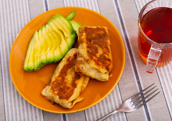 Appetizing baked pancakes stuffed with liver and egg served with avocado on plate