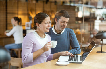 Focused man and woman drinking coffee while working on laptop in cozy cafe