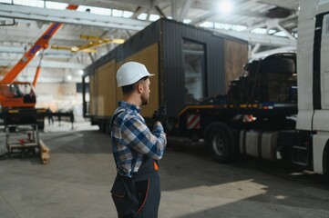 Foreman manages the loading of a prefabricated modular house to truck using walkie talkie