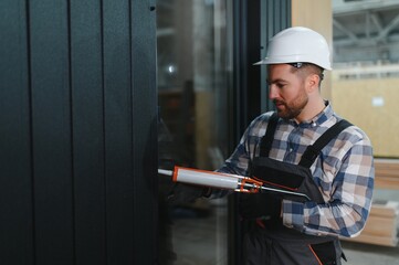 A worker with a silicone gun fills gaps after installing windows in a modular home