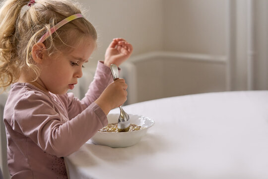 Cute todler girl focused, holding spoon and eating homemade soup at the dining rable with copy space    