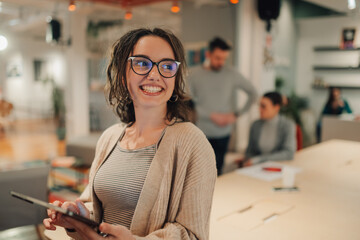 Smiling businesswoman using digital tablet in modern office with colleagues working in background