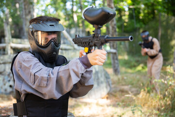 Excited paintball player in protective uniform aiming and shooting with guns