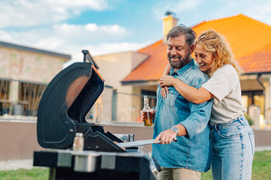 Happy couple grilling and enjoying a beer in their backyard