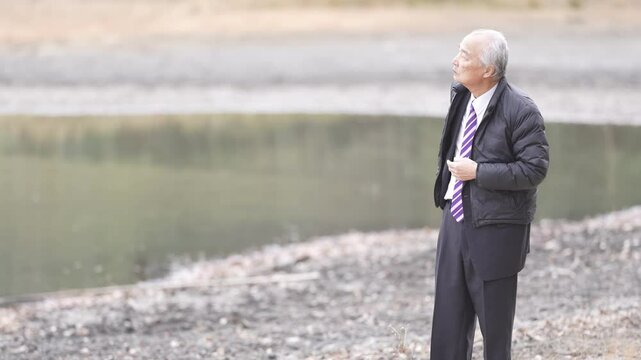 There is a lot of greenery in the bamboo forest pond at noon in spring in Japan. Japanese men in the late 70s stood in suits and down jackets. His son is taking a commemorative photo.