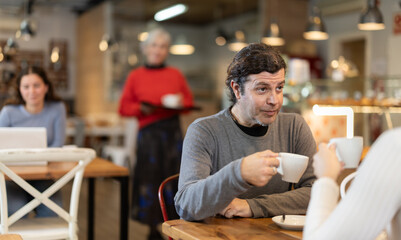 During lunch break, man at cafe drinking coffee, talks with woman, spends time in company of friend. Meeting on neutral territory, discussing personal and business issues