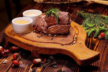 Juicy Round Steak on Wooden Board with Two Sauces, Fresh Rosemary, and Black Pepper, Ideal Photo for Restaurant Menu, Gastronomic Blog, or Steakhouse Advertising.