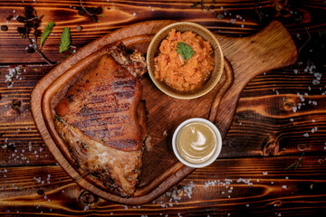 Juicy roasted pork knuckle with garnish on a wooden board, top view