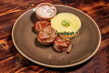 High Angle View: Bacon Wrapped Beef Medallions with Puree and Mushroom Sauce on Textured Plate, Dark Wooden Background