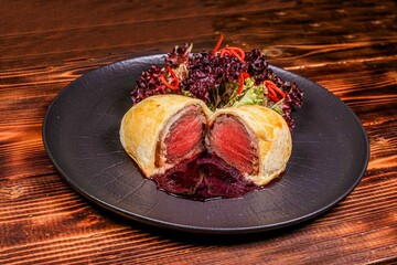 Gourmet Beef Wellington with perfect cut, angled view on dark wooden background.