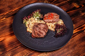 Premium grilled steaks with interesting side dish, angled view on dark wood.