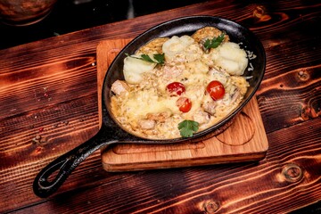 Hot baked meat with cheese and potatoes in cast iron skillet, angled view on wood.