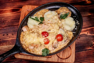Hearty baked meat with cheese and potatoes in skillet, top view on wooden table
