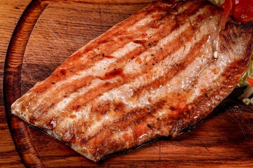 Close up: Appetizing grilled fish with marks on rustic wooden cutting board.