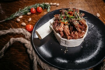 Culinary Creation: Top View of Meat with Vegetables in Lavash, Garnished with Sesame Seeds and Chili, on Black Plate with Natural Wooden Background.