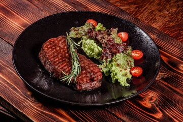 Appetizing Grilled Steak with Rosemary and Fresh Salad on Black Plate, Presenting an Exquisite Combination of Flavors on Wooden Table.