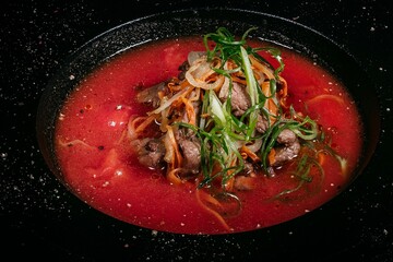Refreshing Gazpacho, Skillfully Garnished with Meat and Vegetable Julienne on Black Plate Background, Evoking Culinary Delight, Top View.