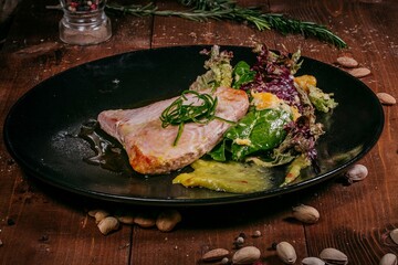 Tuna steak with greens and mango sauce on a black plate, top view, wooden background