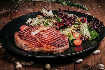 Grilled steak with salad and tomatoes, side view on wood