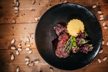 Juicy grilled steak with vegetable salad on black plate, top view, rustic wooden background