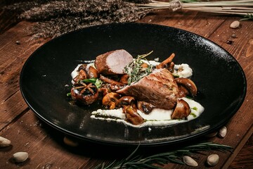 Appetizing Pork Tenderloin, Roasted with Forest Mushrooms and Tender Mashed Potatoes, Served on Stylish Black Plate, Decor of Herbs and Spices, Serving on Wooden Background.
