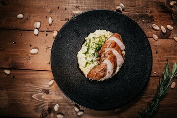Top View: Exquisite Chicken with Risotto on Dark Plate, Decorated with Greens, Decor of Spices and Nuts on Wooden Table, Elegant Serving and Gourmet Pleasure.
