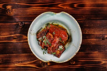 Braised meat in tomato sauce with herbs and garlic, vintage plate, top view, wooden background