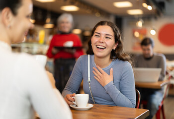 During lunch break, girl at cafe drinking coffee, talks with female interlocutor, spends time in company of friend. Meeting on neutral territory, discussing personal and business issues