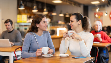Two friends are chatting happily with each other while sitting at table in a cafe and drinking tea