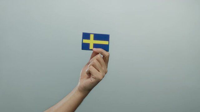 Caucasian man hand holding swedish flag embroidery against isolated white wall background.