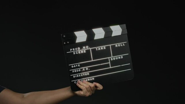 Man holding film clapperboard against black background signifies filmmaking and production process.