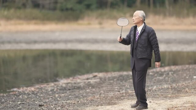 At noon in spring in Japan, there is a lot of greenery in the bamboo forest pond. Japanese men in the late 70s stood in suits and down jackets. He plays badminton with his son in his 30s.