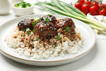 Delicious rice with meatballs, sauce and green onions on white table, closeup