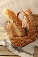 Different loaves of fresh bread in basket on wooden table, closeup