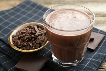Tasty chocolate milk with shavings and pieces on wooden table, closeup