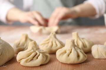Woman making khinkali on table in kitchen, closeup