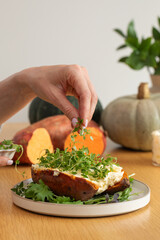 Hand garnishing stuffed sweet potato with fresh herbs on table. Healthy food